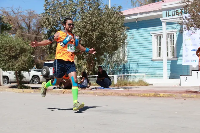 Corredor con polera naranja y medias verdes frente al edificio municipal en Huara Desert 2015.