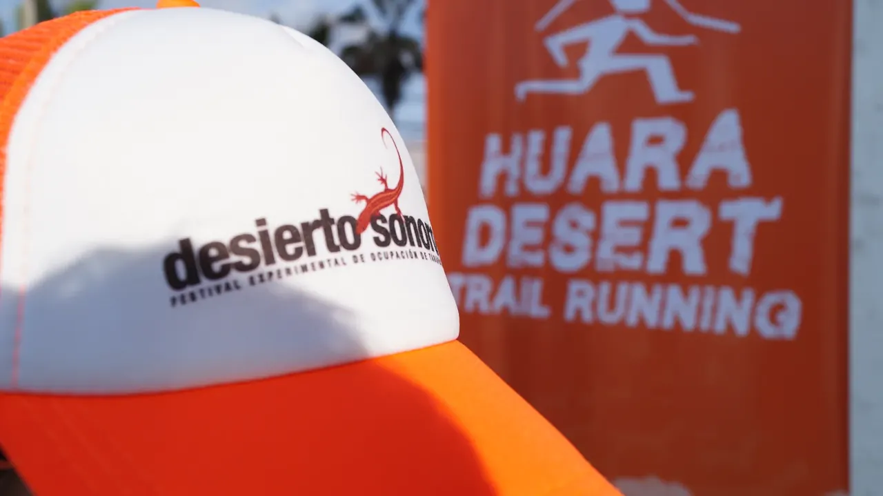 Gorro naranja y blanco junto a un pendón naranja de Huara Desert Trail Running.