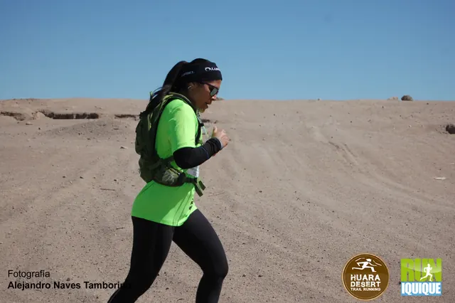 Corredora con polera verde y mochila avanzando por una ruta de tierra en Huara Desert 2016.