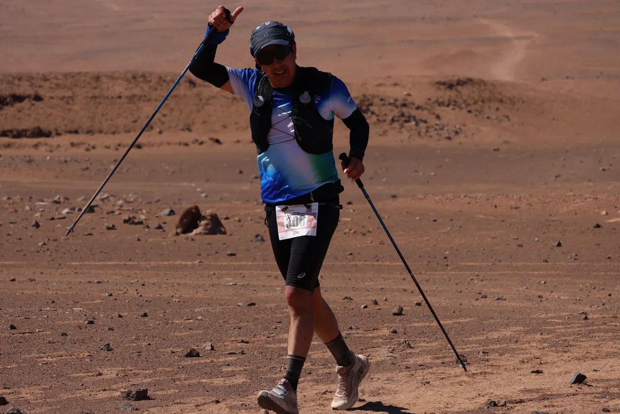Deportista con bastones saluda a la cámara en una pendiente rojiza