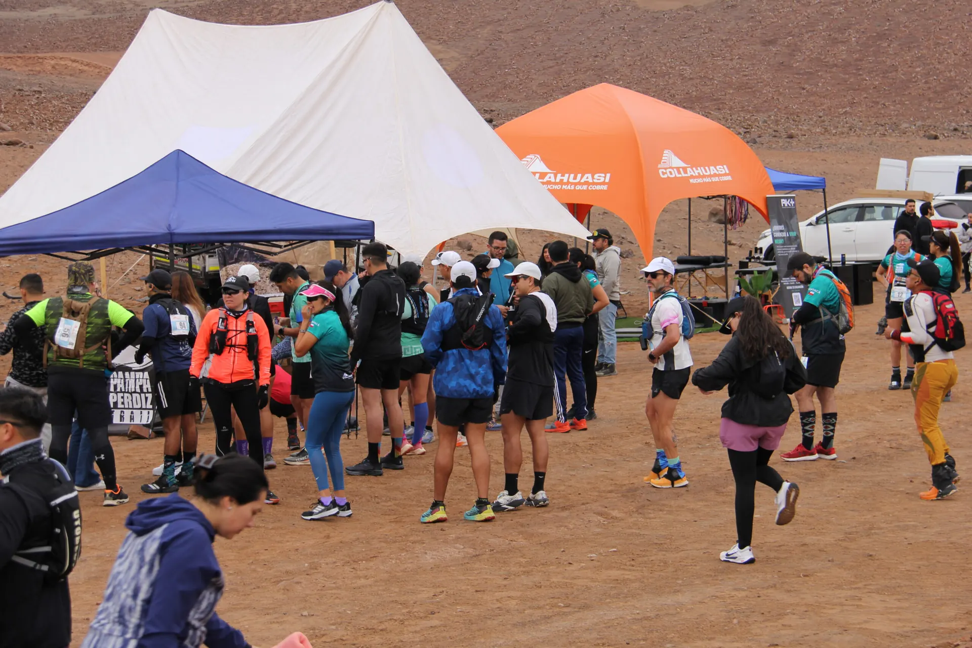 Campo base de un evento en el desierto con carpas, banderas de auspiciadores y corredores
