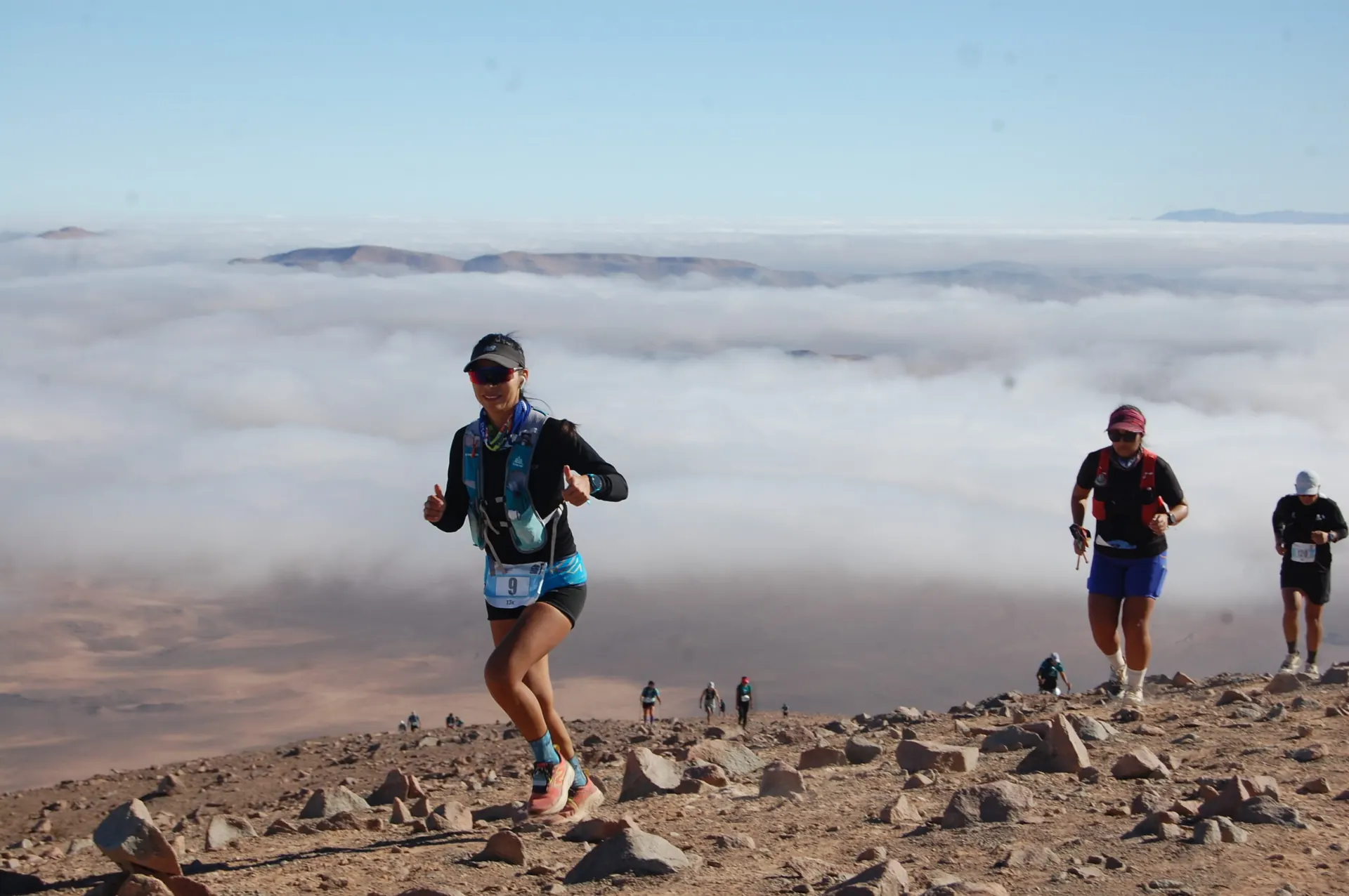 Corredores en una ladera de piedras con el mar de nubes de la costa de Tarapacá detrás